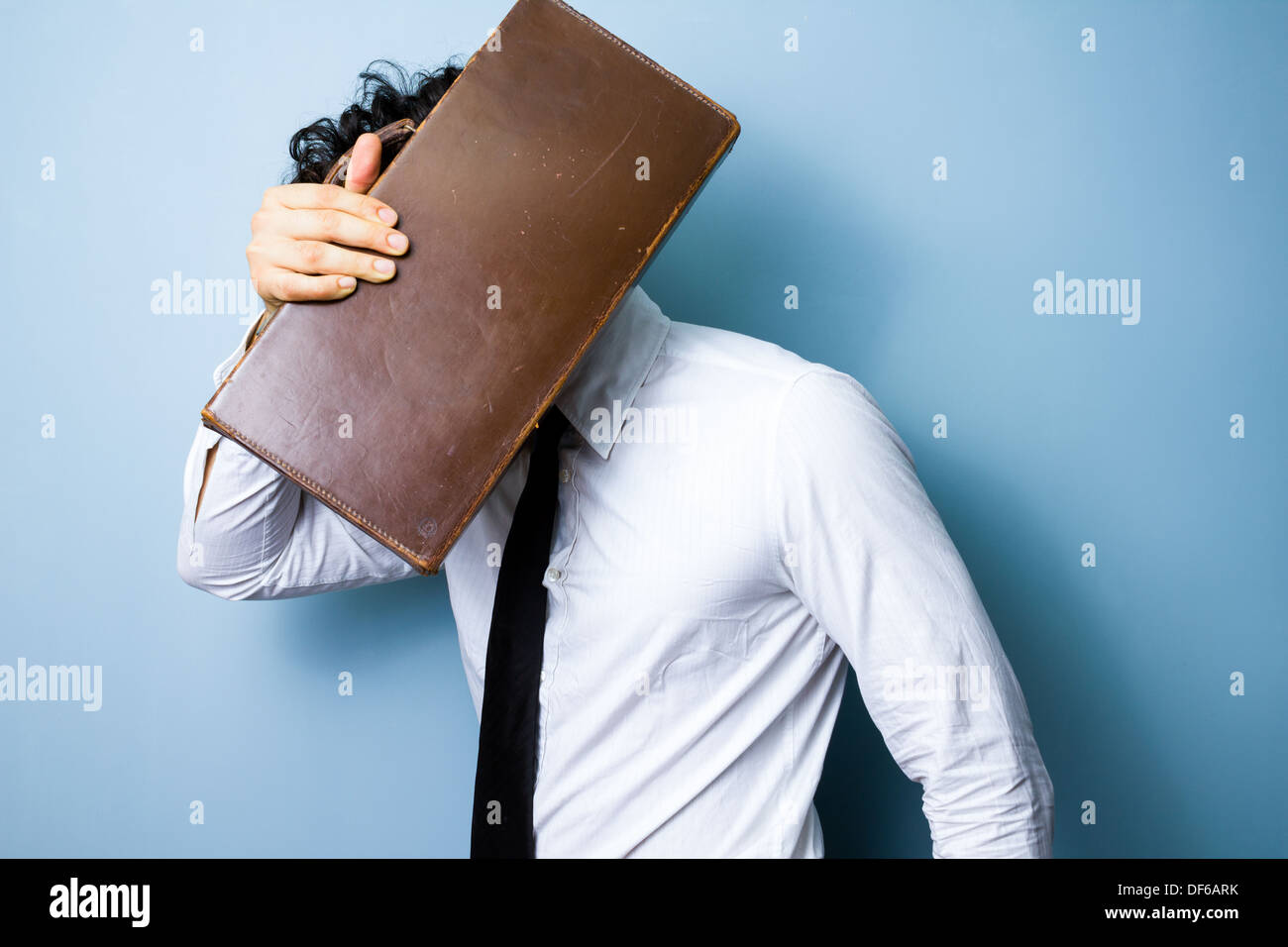 Young businessman is hiding his face behind a briefcase Stock Photo