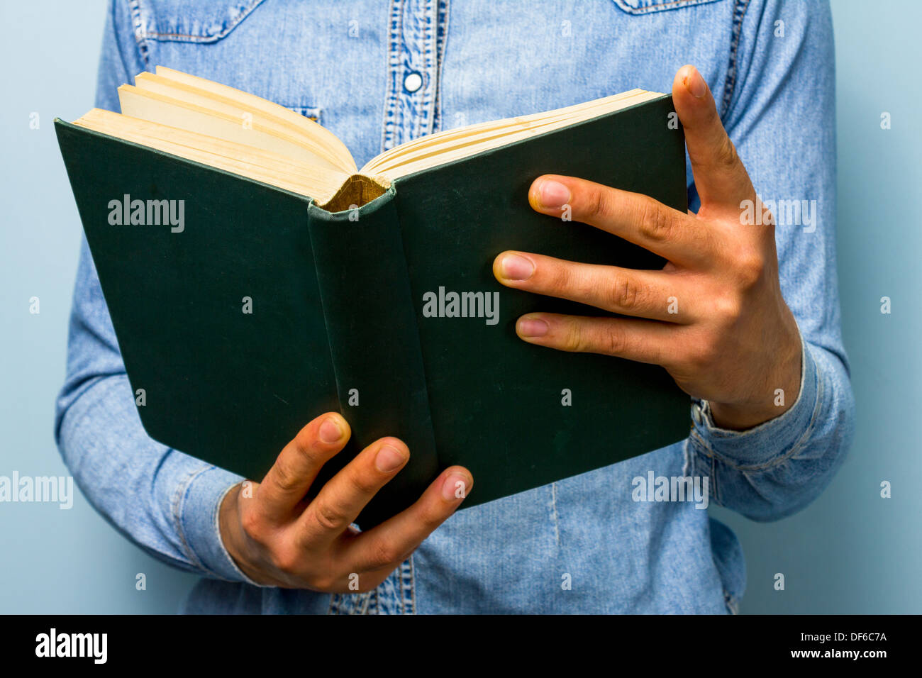 Young blue collar worker is reading a big heavy book, perhaps the Bible Stock Photo