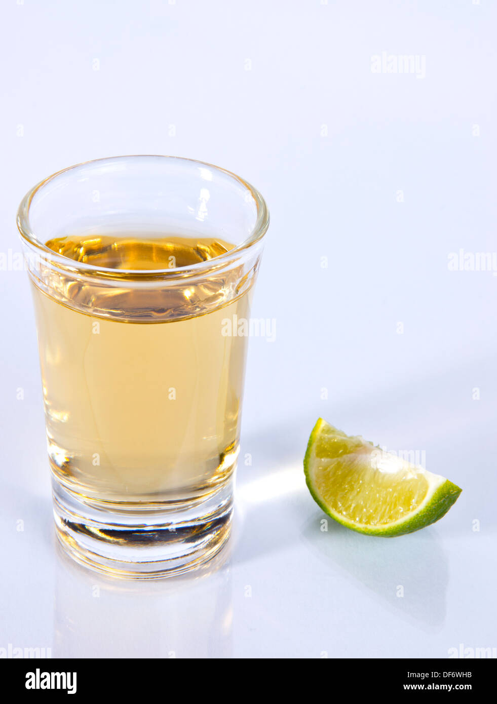 Tequila Shot with Quarter Green Lime on Reflective Foreground and White Background Stock Photo
