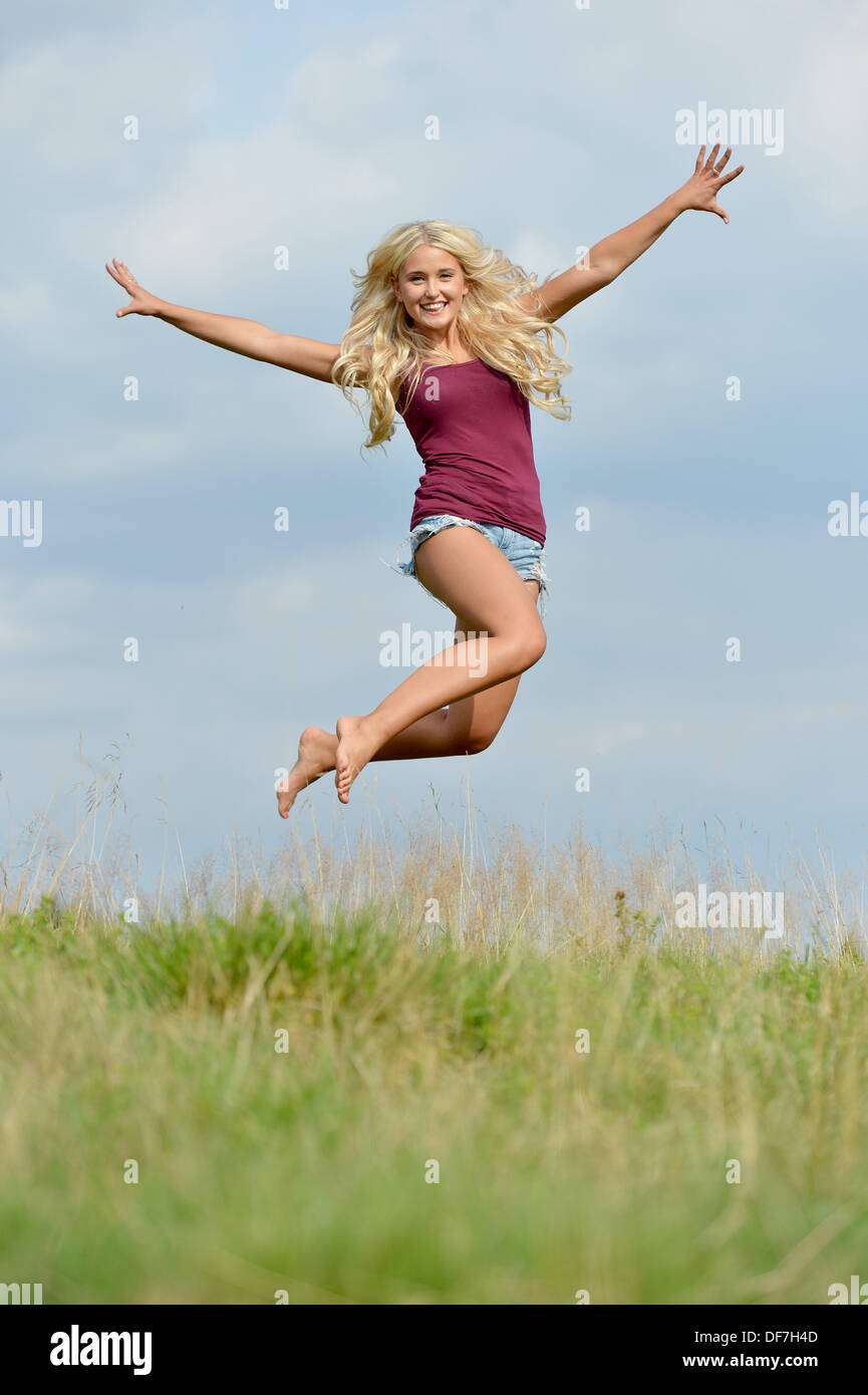 A young blonde woman is jumping up with joy. Stock Photo
