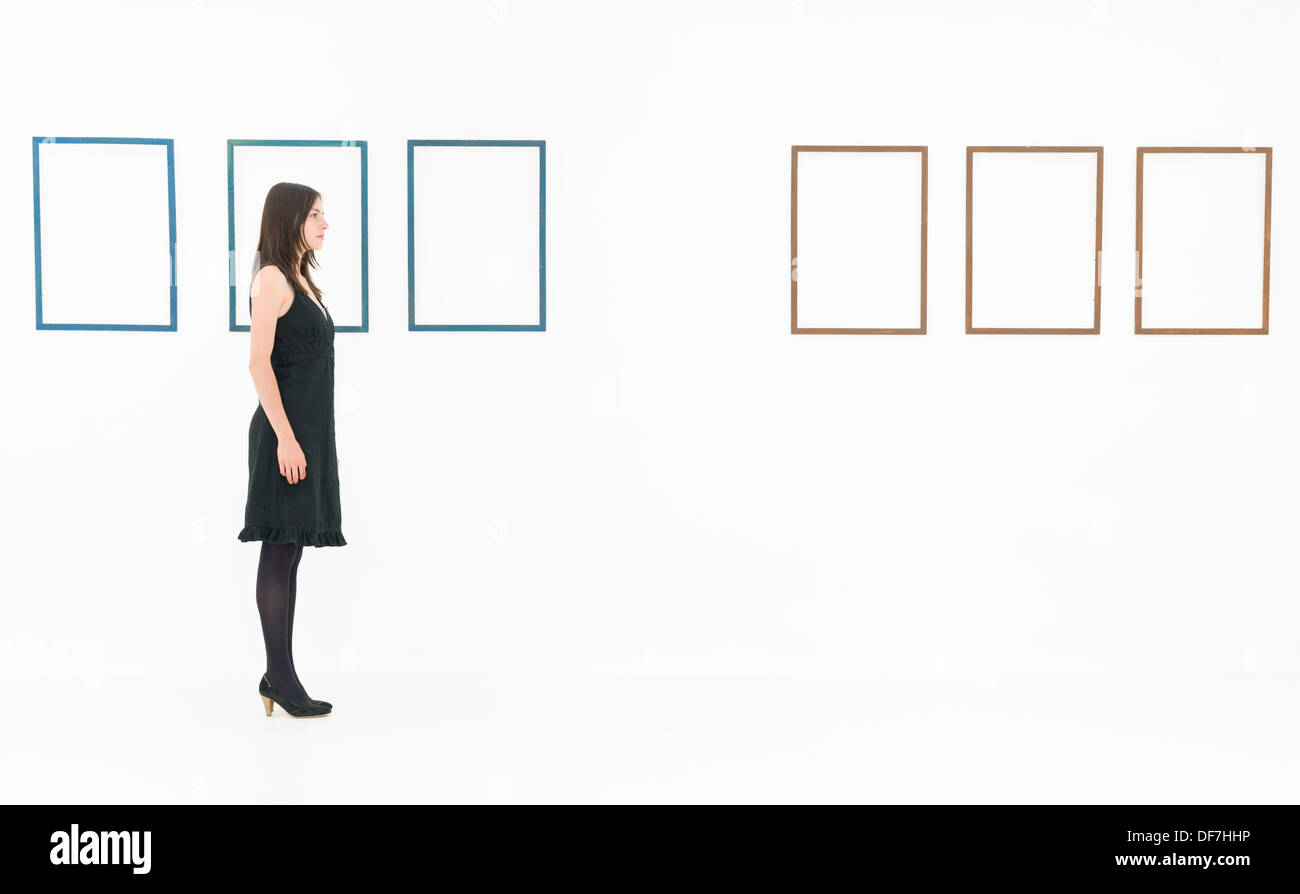 side view of woman standing in a white room near empty frames Stock Photo