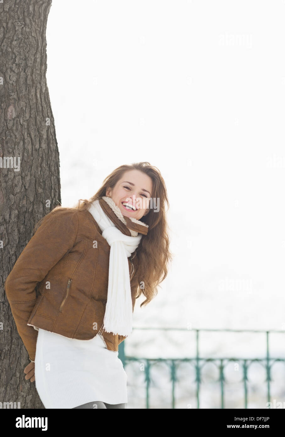 Happy young woman leaning against tree in winter park Stock Photo
