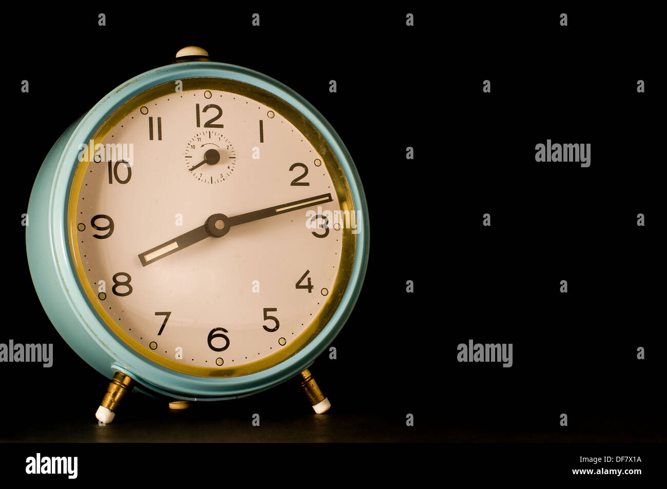 Old alarm clock showing twelve past eight on black background. Stock Photo