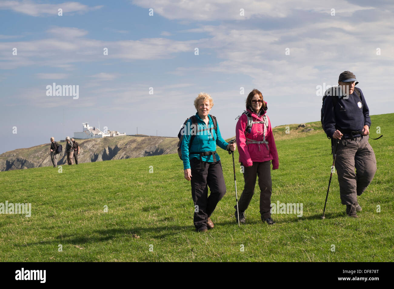 Seniors walking on coastal path with Point Lynas lighthouse beyond in Llaneilian, Isle of Anglesey, North Wales, UK, Britain Stock Photo