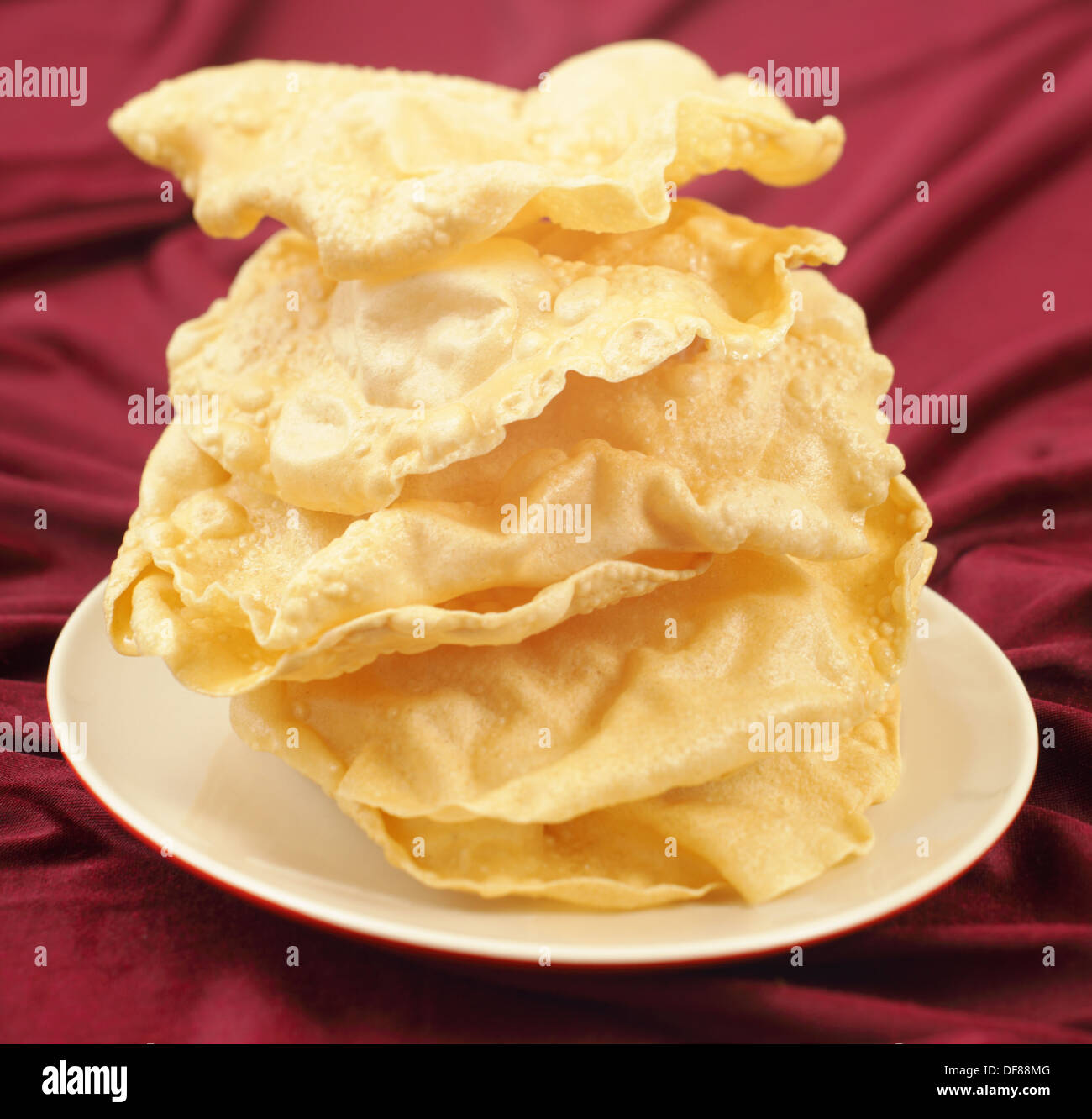 A pile of poppadoms on a plate resting on a red cloth. Stock Photo