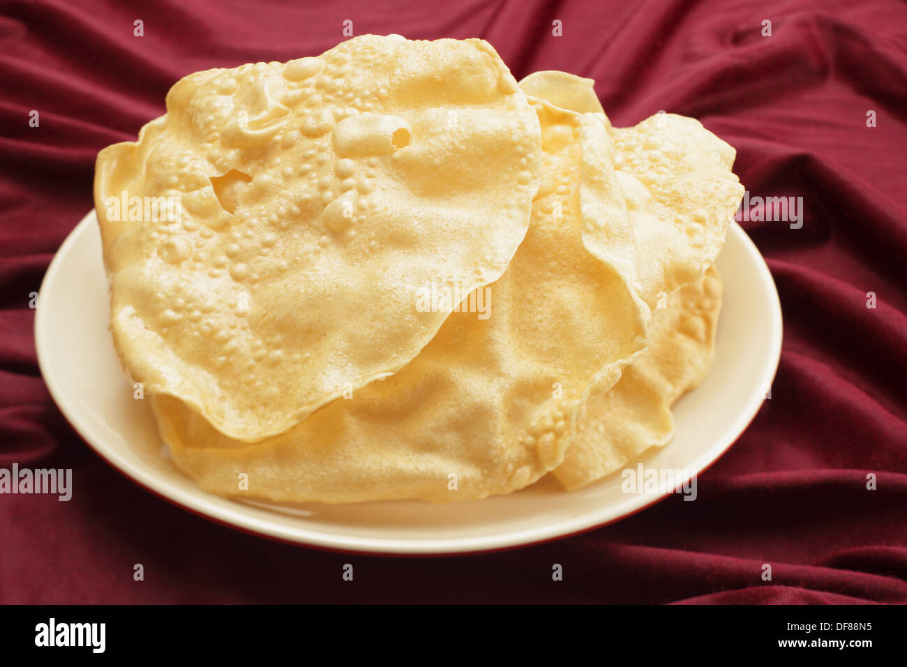 A pile of poppadoms on a plate resting on a red cloth. Stock Photo