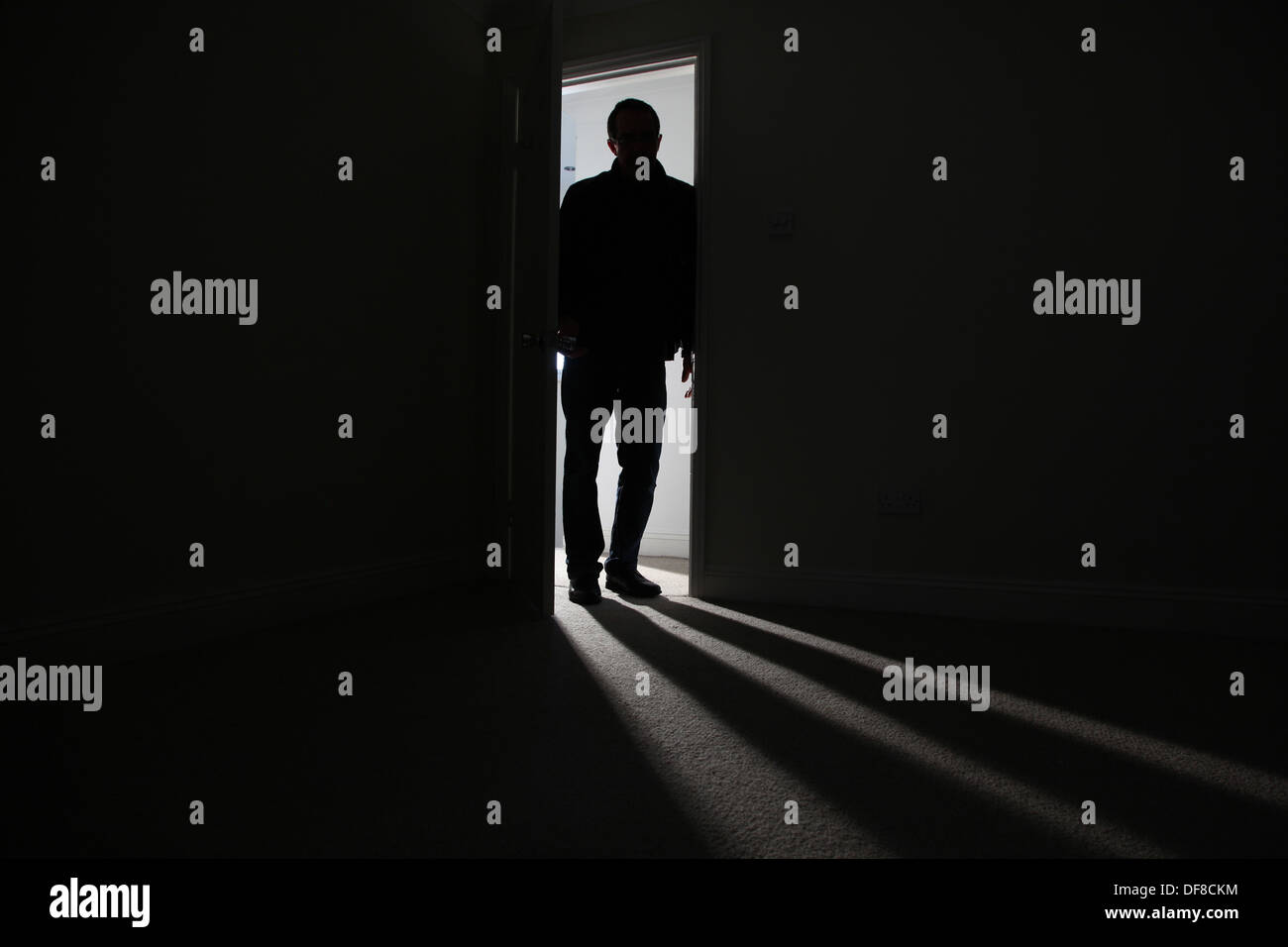 Silhouette of a male adult standing in an open doorway, entering a dark room. Model released Stock Photo