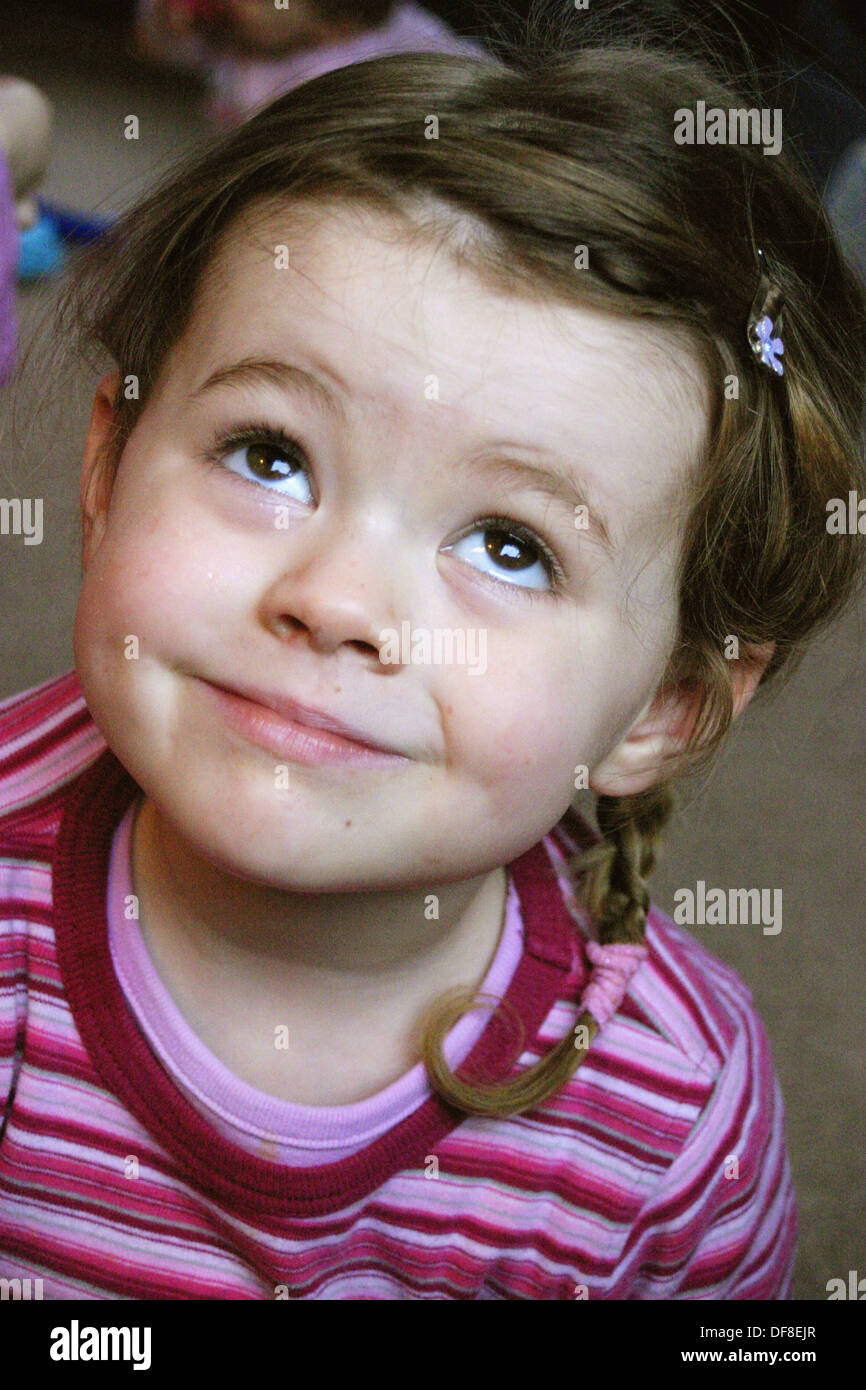 Headshot of 3 year old girl, with plaits and stripey top, looking up Stock Photo