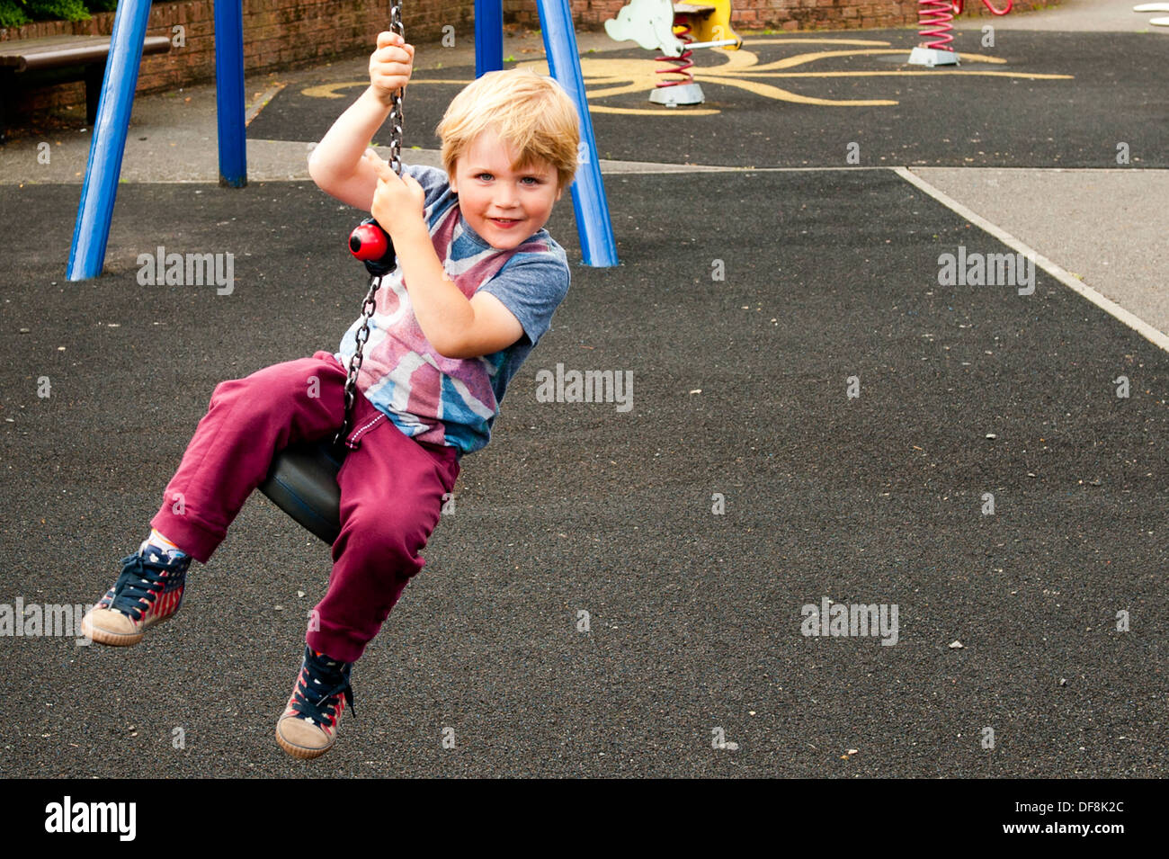 boy at play park having fun sitting on death slide wearing union flag t shirt Stock Photo