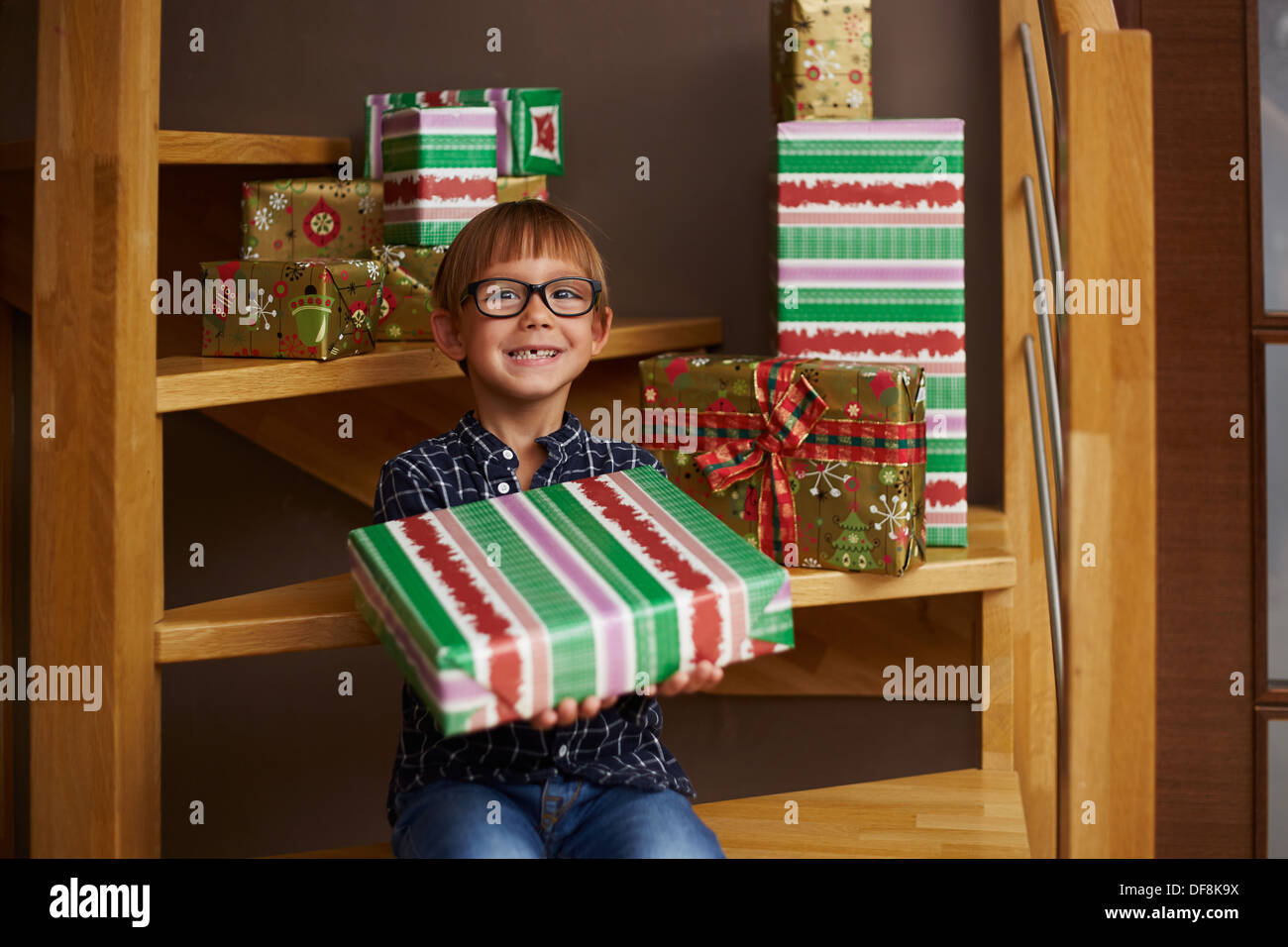 Smiling boy ready to open Christmas presents on the stairs of his house Stock Photo