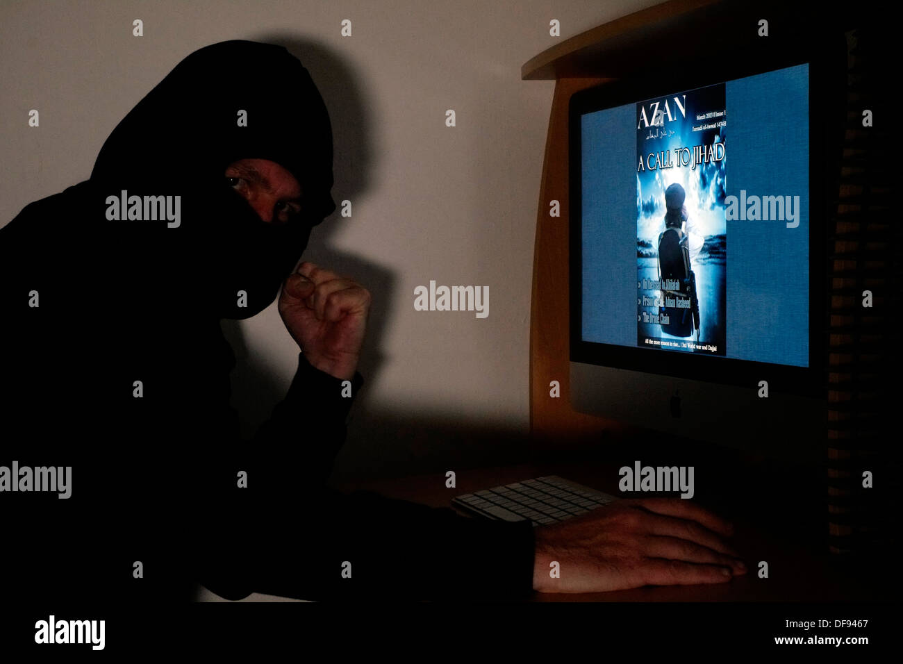 hooded and masked man looking at the terrorist magazine azan on line on his computer Stock Photo