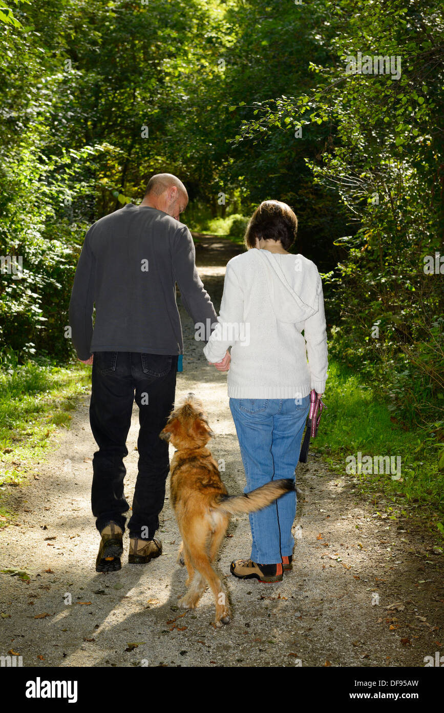 Couple holding hands and walking a dog off leash on a woodland path in a forest Park of Toronto Stock Photo