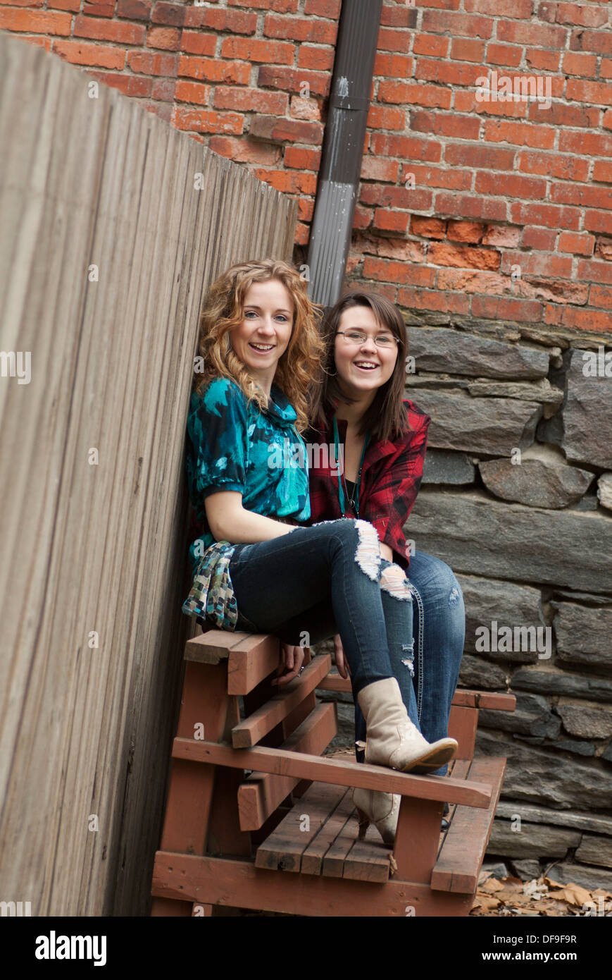 Two young women sitting outdoors together and laughing Stock Photo - Alamy