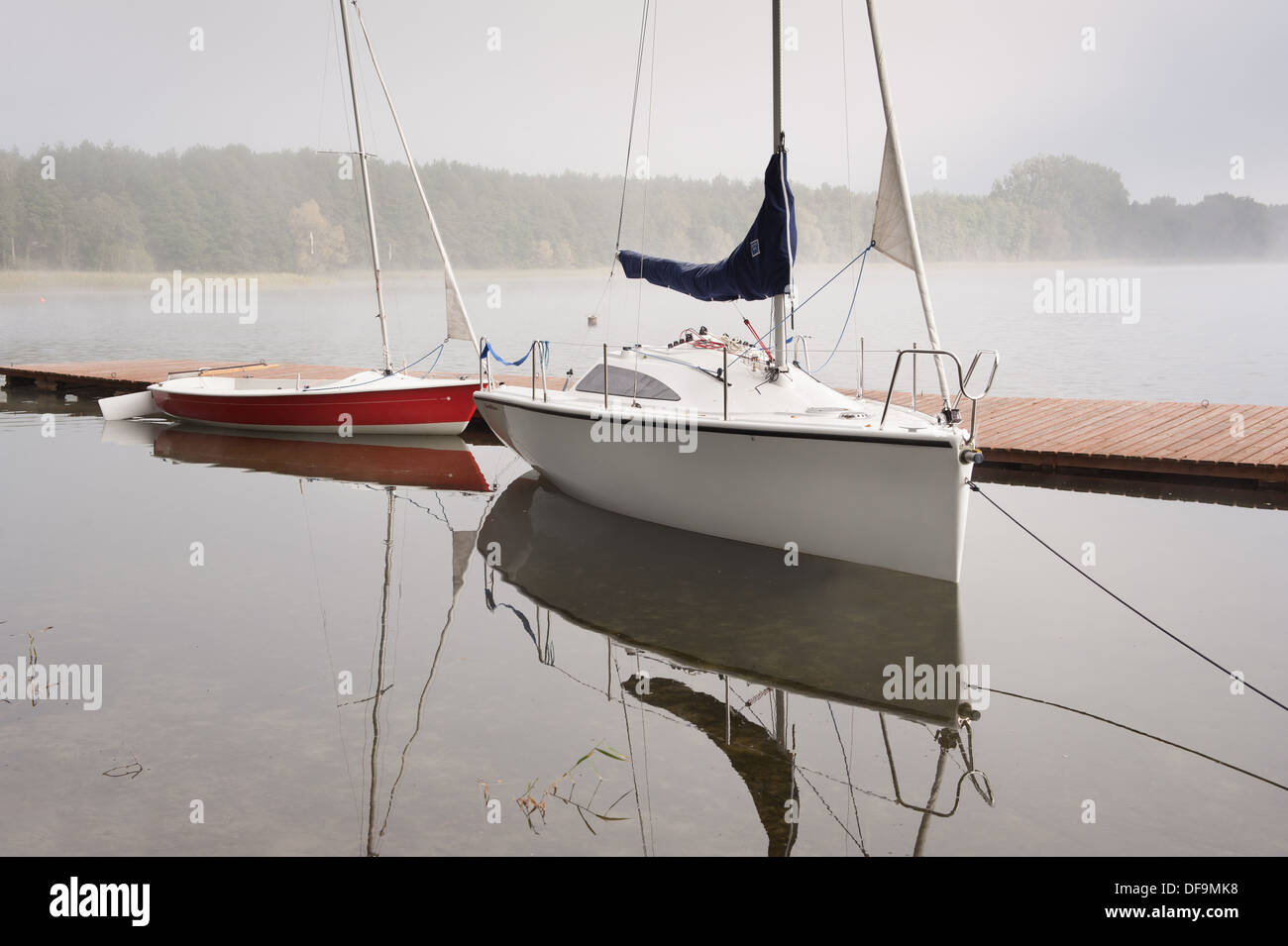 Two boats in fog moored to boardwalk at lake Stock Photo