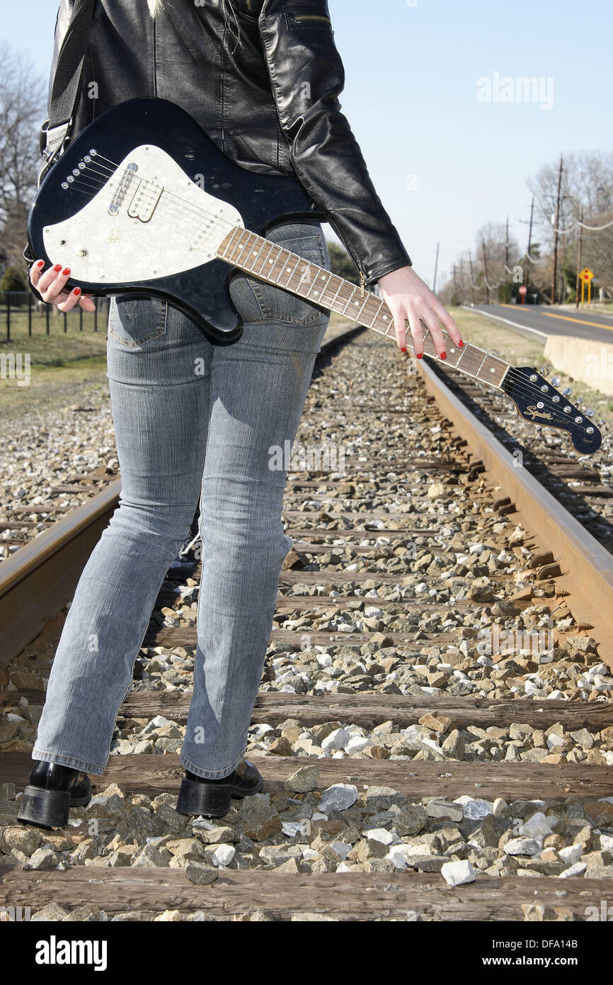 Young woman carrying a guitar standing on railroads looking into and