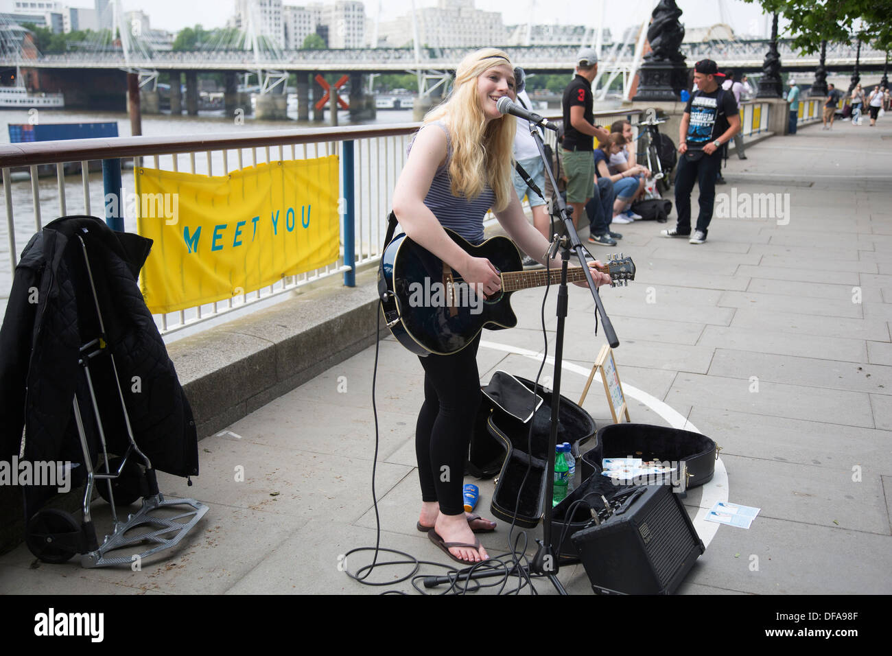 Young busker (Charlotte Campbell) performing her music, both singing and playing guitar on the Southbank. South Bank is a significant arts and entertainment district, it's riverside walkway busy with visitors and tourists. London, UK. Stock Photo