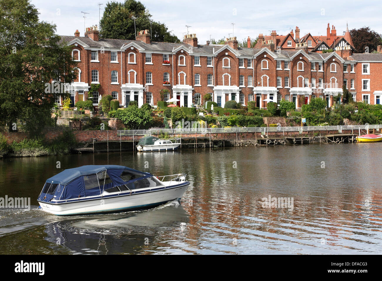 A small cabin cruiser sails past a terrace of houses on the banks of the River Dee in
