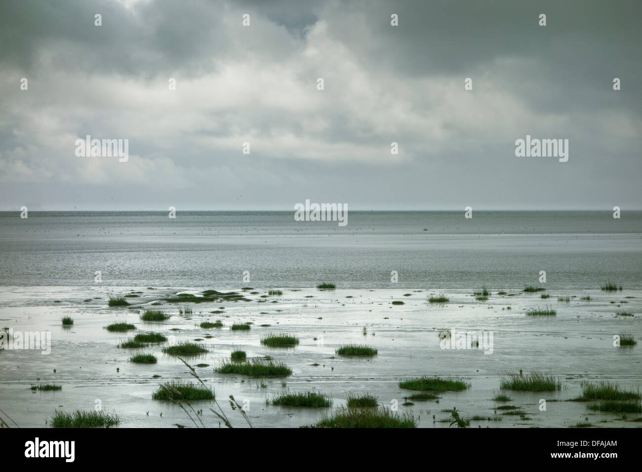 Dark grey stormy clouds, over an incoming tide. Stock Photo