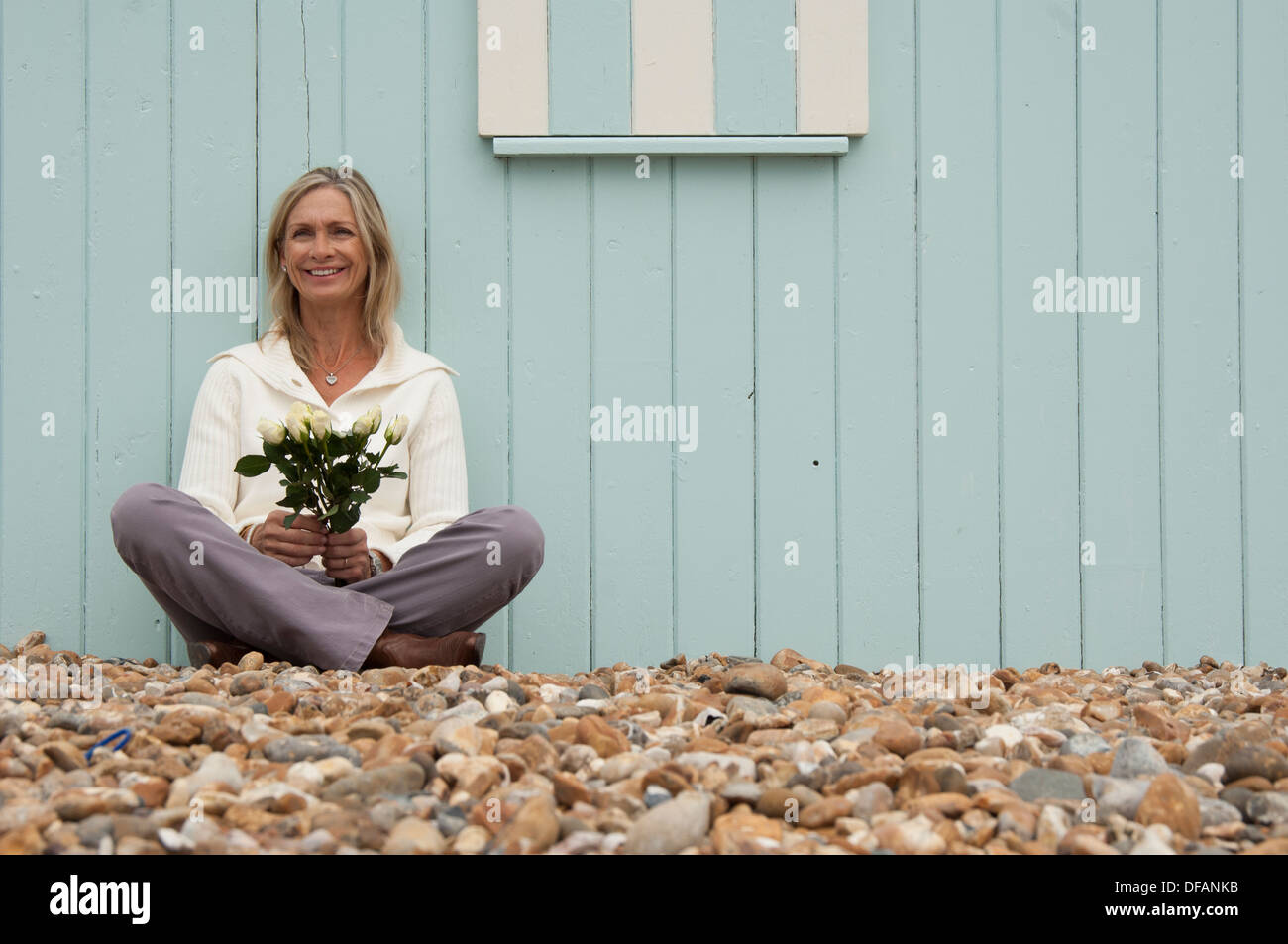 mature woman sitting on the beach holding a bunch of flowers Stock Photo