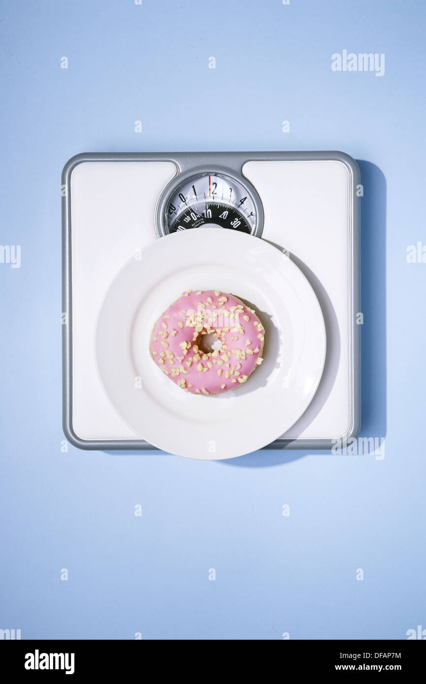 Pink iced donut on bathroom scales. Stock Photo