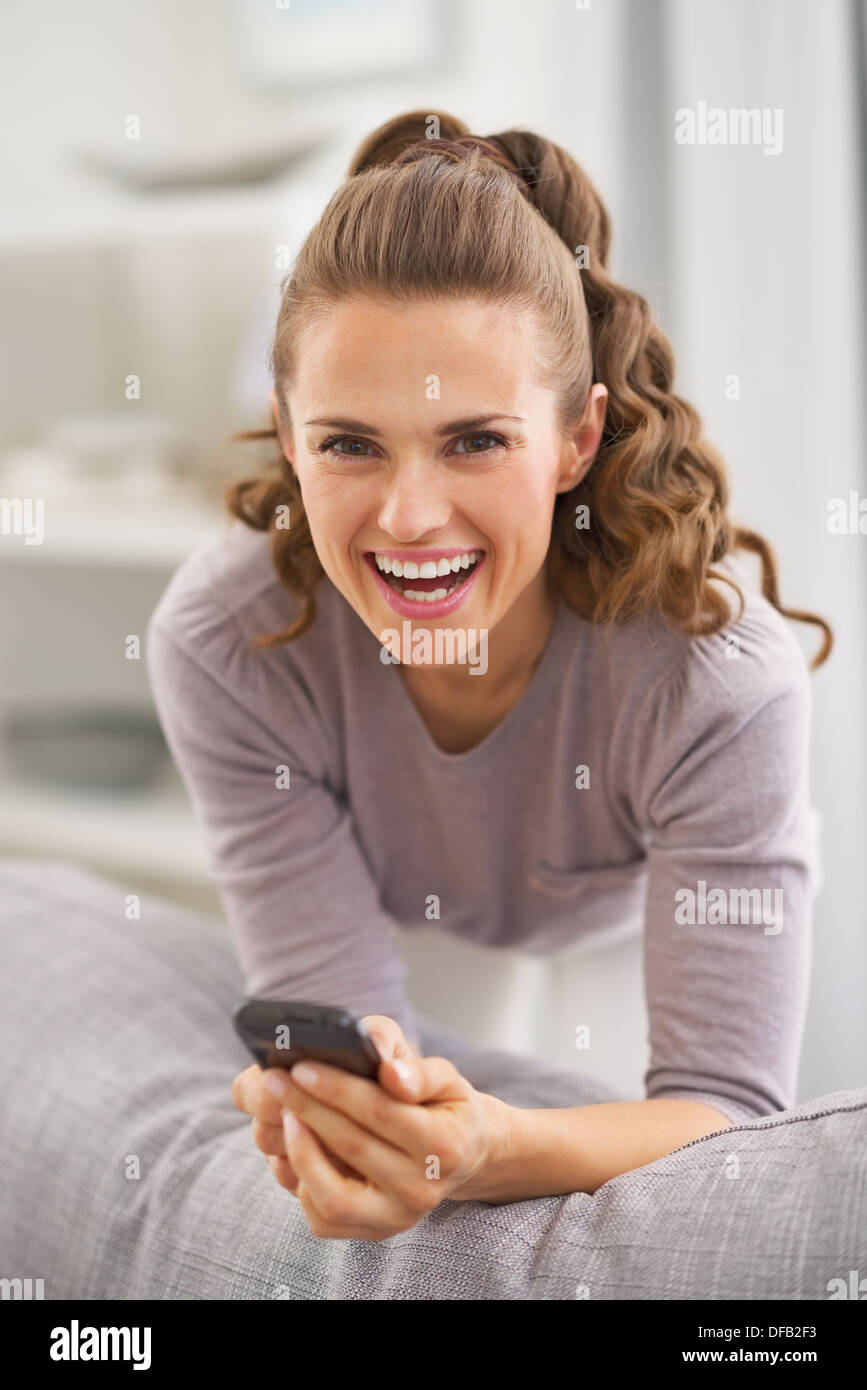 Smiling young woman with mobile phone in living room Stock Photo