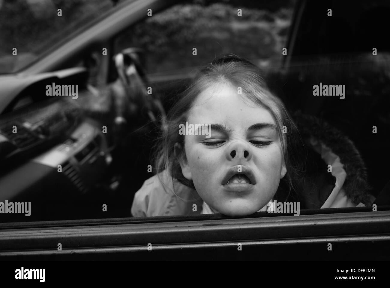 Girl pressing nose against car window whilst winding it up to make funny face Stock Photo