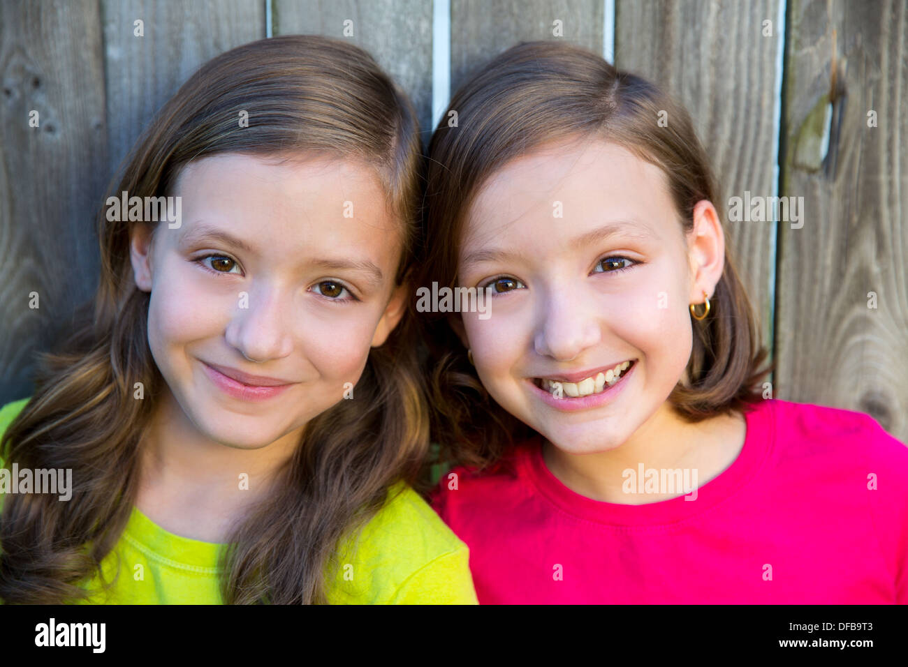 Happy twin sisters with different hairstyle smiling on wood backyard fence Stock Photo