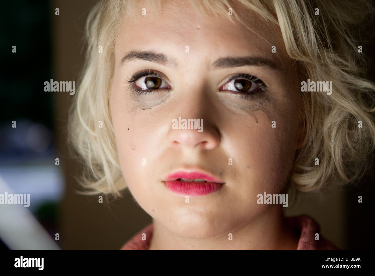 !9 year old blond female face closeup with tears and runny makeup visibly in emotional distress, sad, looking straight into you Stock Photo