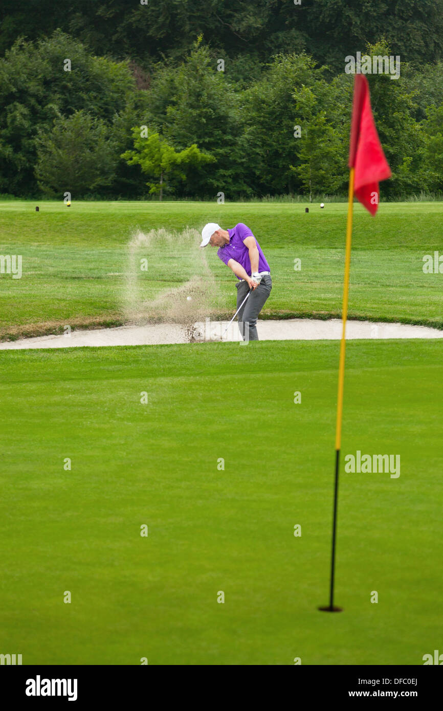 A professional golfer hitting his ball out of a bunker with the sand and ball in mid-air. Stock Photo