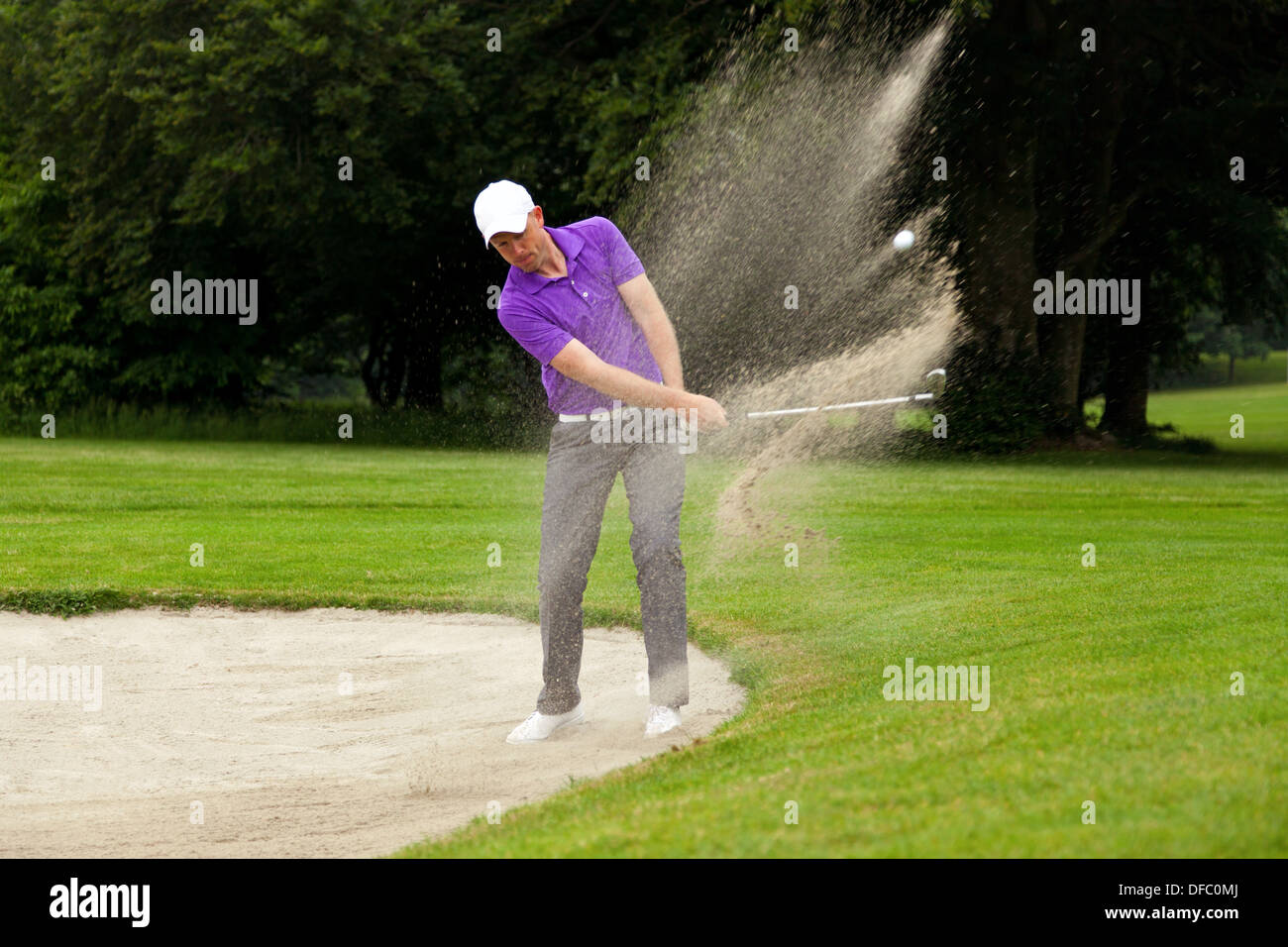 A professional golfer hitting his ball out of a bunker with the sand and ball in mid-air. Stock Photo
