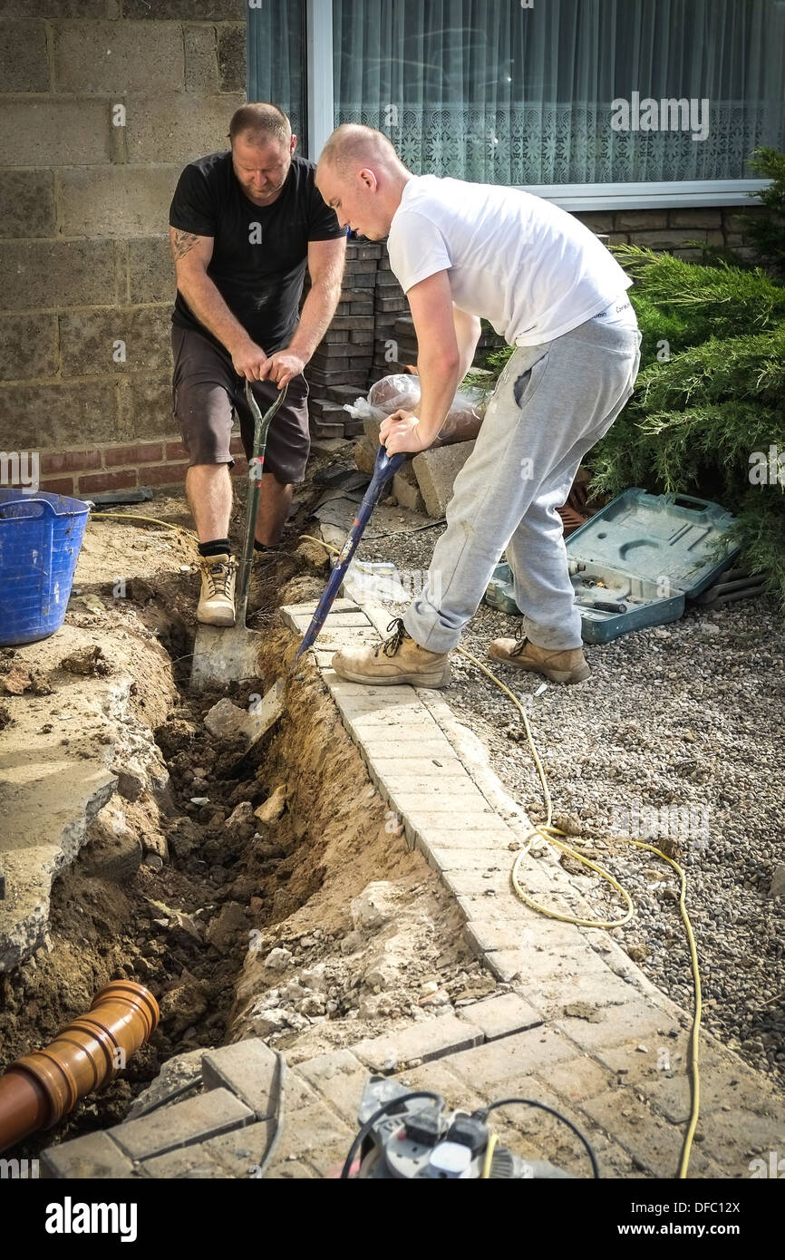 Two builders digging a trench in preparation for laying new drainage pipes. Stock Photo