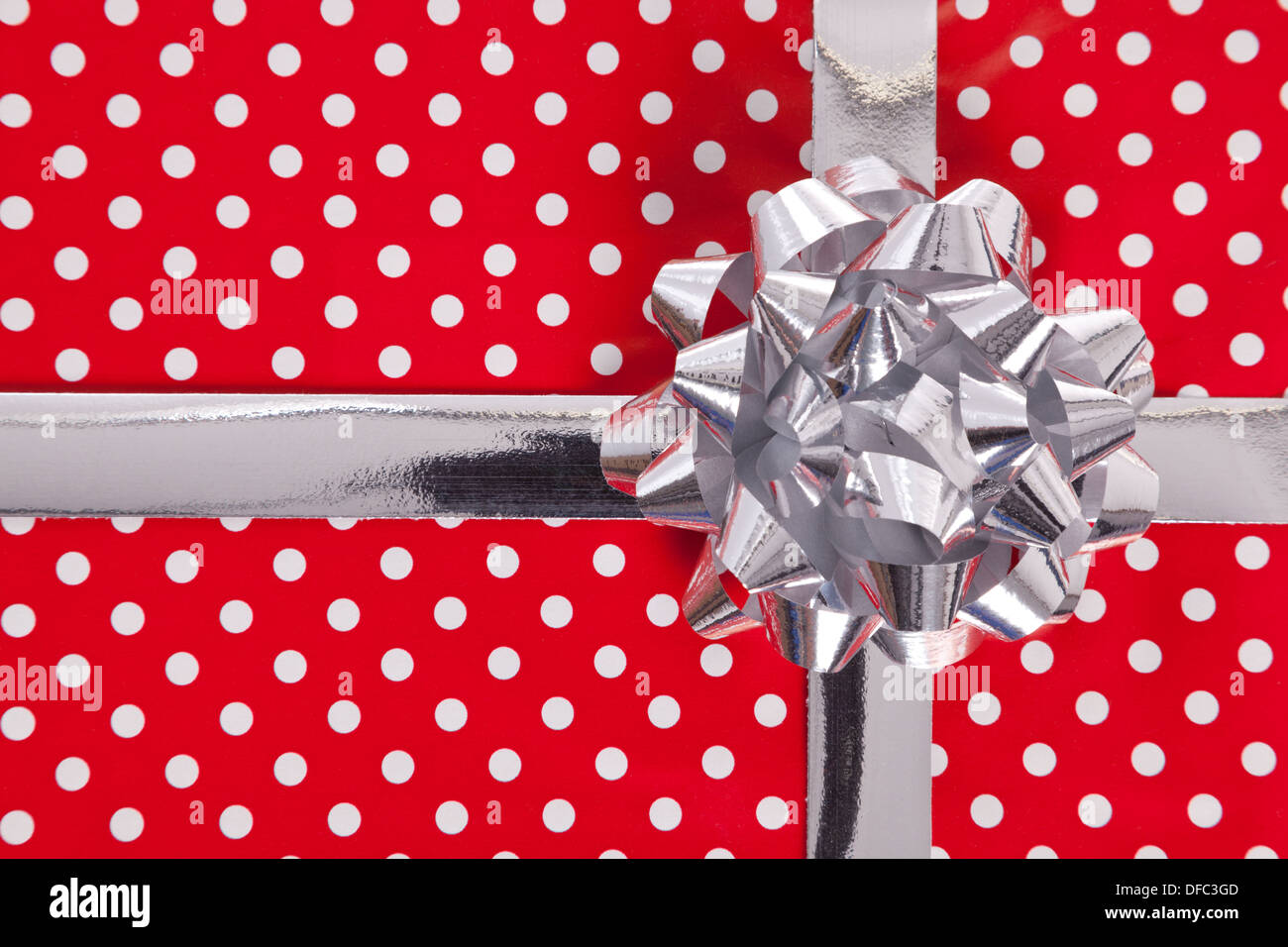 Red polka dot gift paper with silver bow and ribbon. Stock Photo