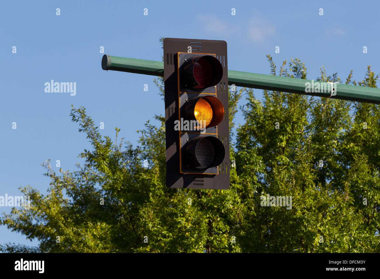 Traffic signal, orange light, amber light, or traffic light.  Blue sky and green trees in the background Stock Photo