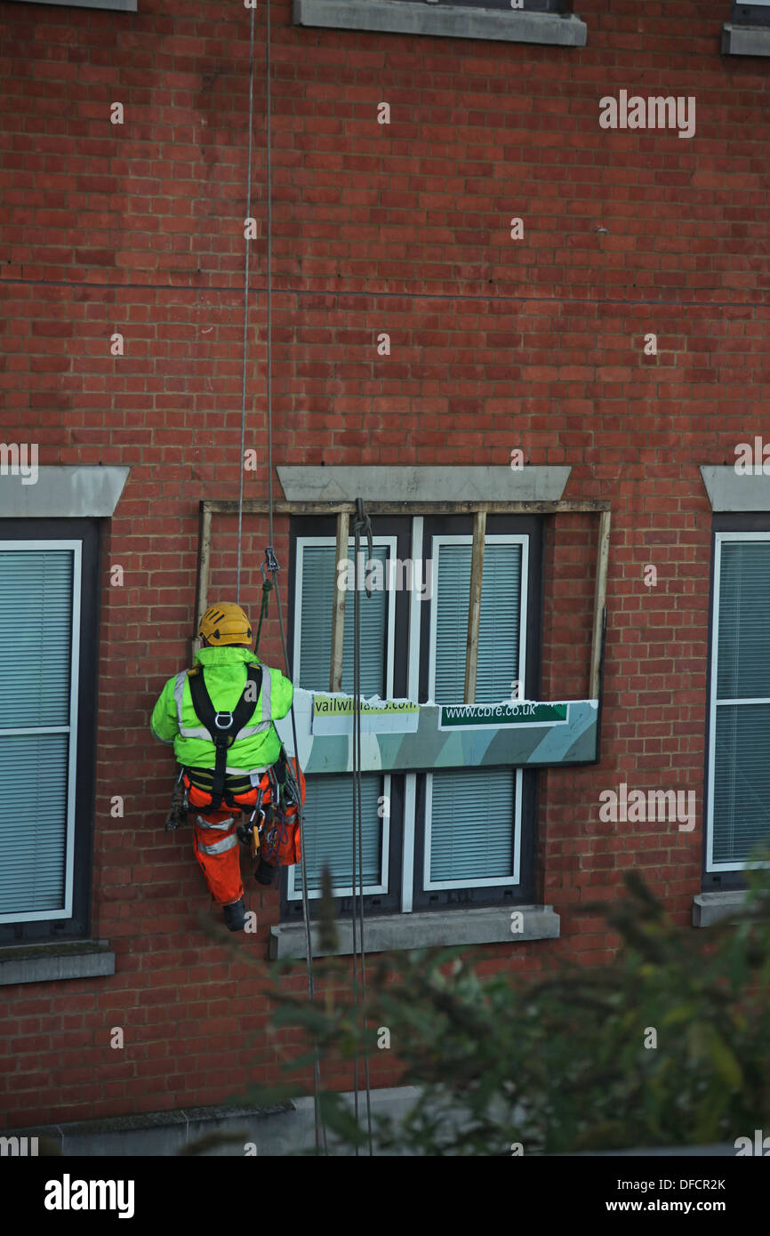 A worker suspended beside a window he is working on removing an old advertising board. Stock Photo