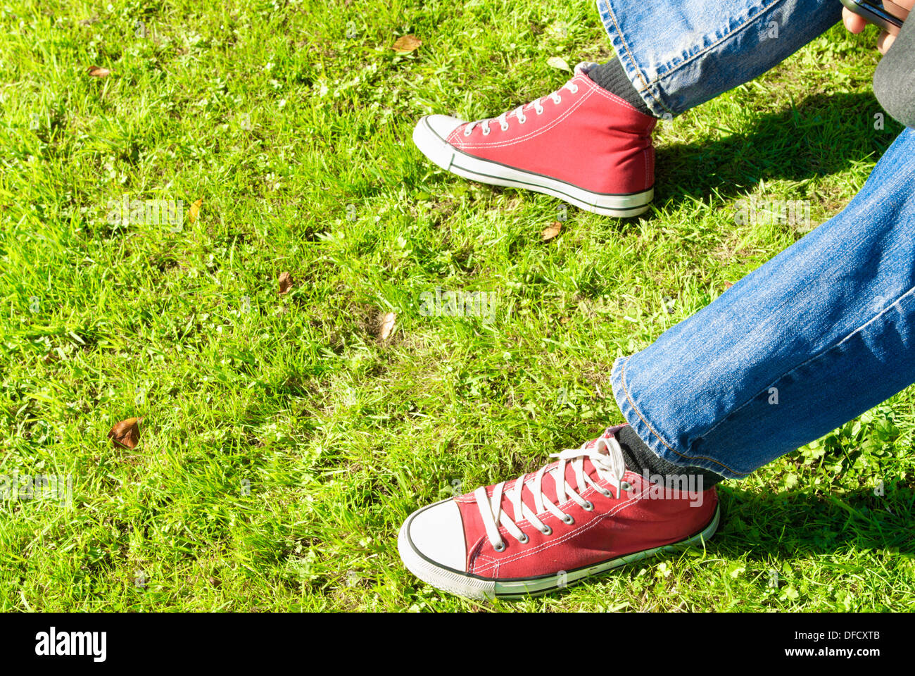 Legs of a young adult relaxing on grass. Mobile phone in hand Stock Photo