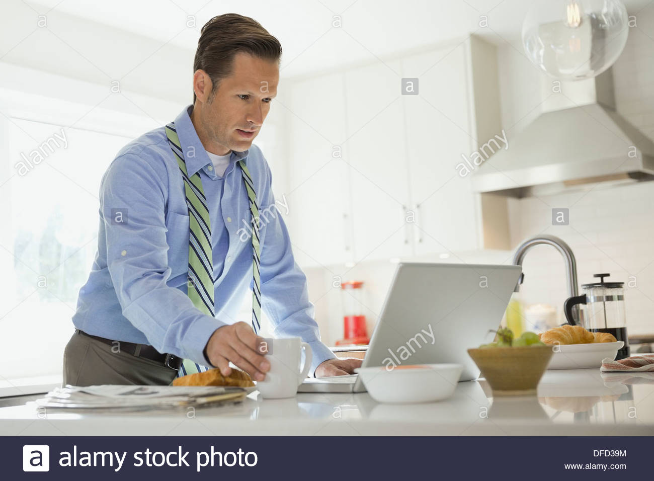 Mature businessman using laptop in domestic kitchen Stock Photo