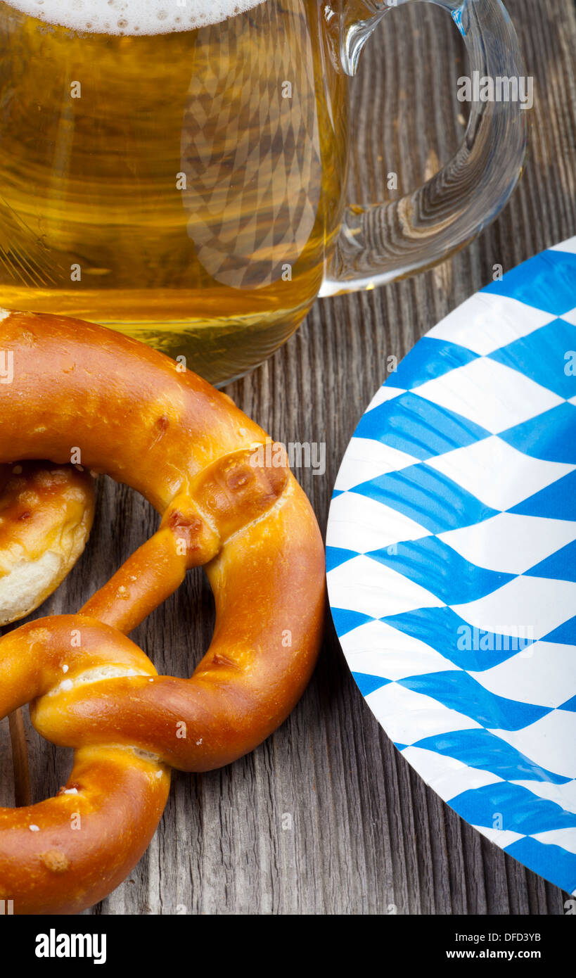 Part of of a beer glass, pretzels and a Paper Plates with blue and white rhombuses on a rustic wooden table Stock Photo