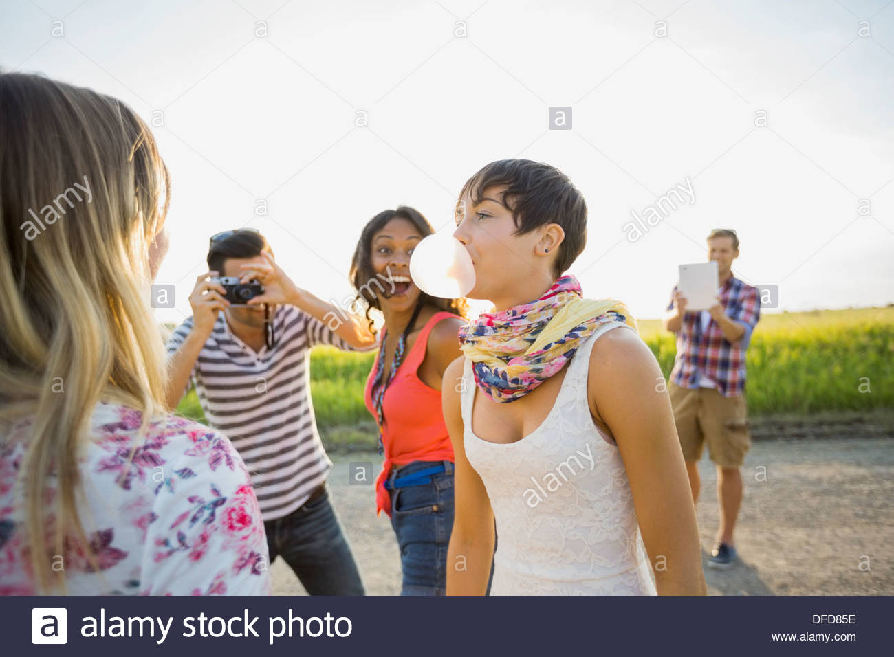 Cheerful friends looking at woman blowing bubble gum Stock Photo