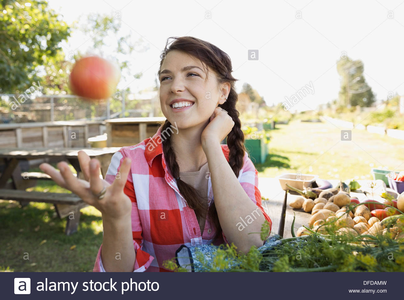 Playful woman tossing apple in community garden Stock Photo