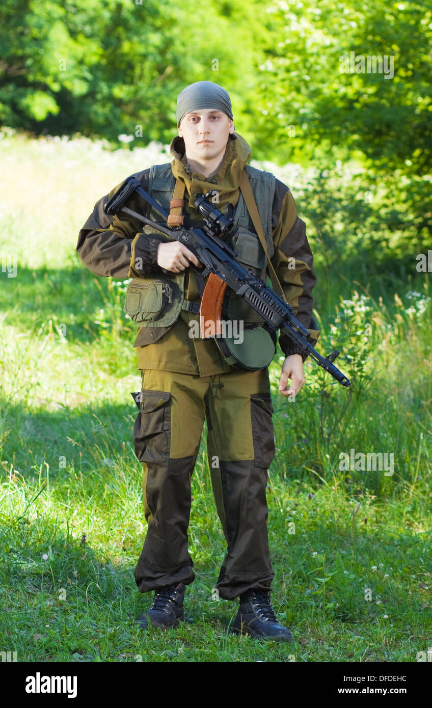 soldier in camouflage with a Kalashnikov assault rifle, standing on grass Stock Photo