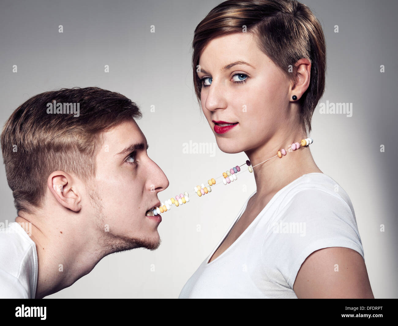 Young man biting candy necklace while woman looking at camera Stock Photo