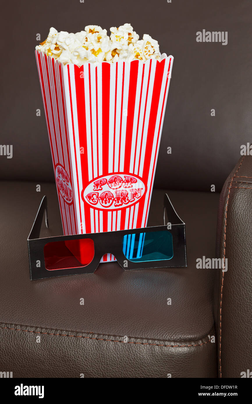 Box of Popcorn with 3D TV glasses on a brown leather home cinema chair. Stock Photo