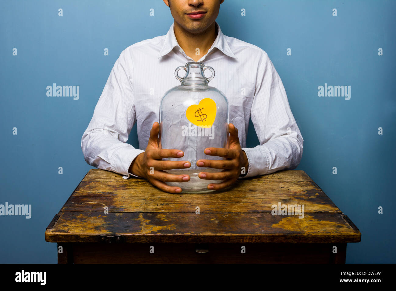 Young man is sitting at an old desk with his empty piggy bank Stock ...