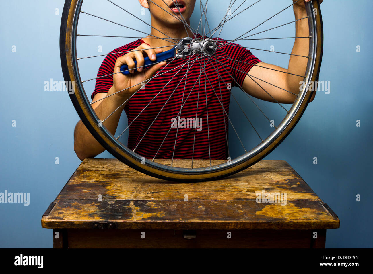 Young man is sitting at an old desk and fixing a bicycle tire Stock Photo