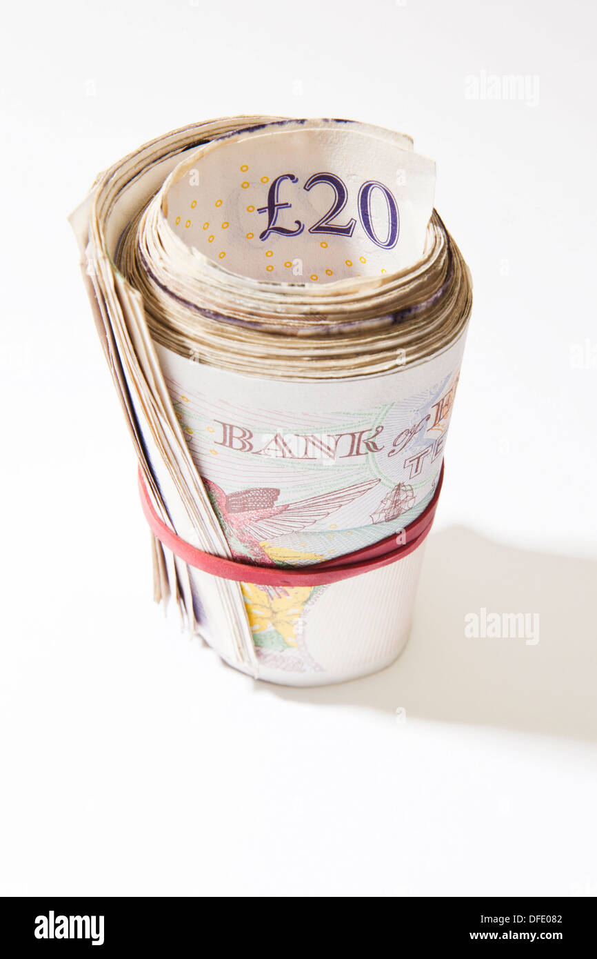 A roll of British notes held together by an elastic band with a plain background. Stock Photo