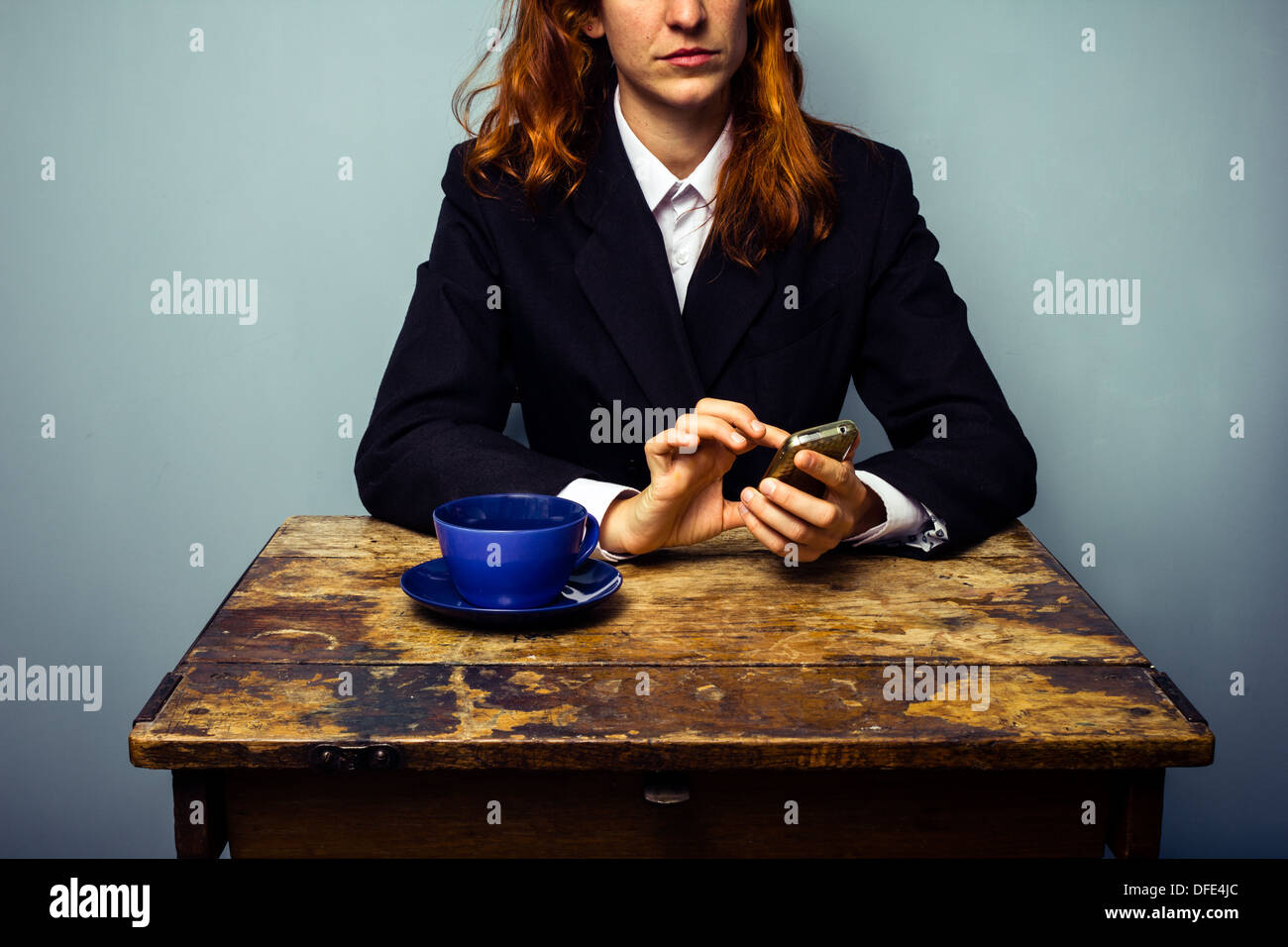 Young business woman is sitting at an old table and texting on her phone while having coffee Stock Photo