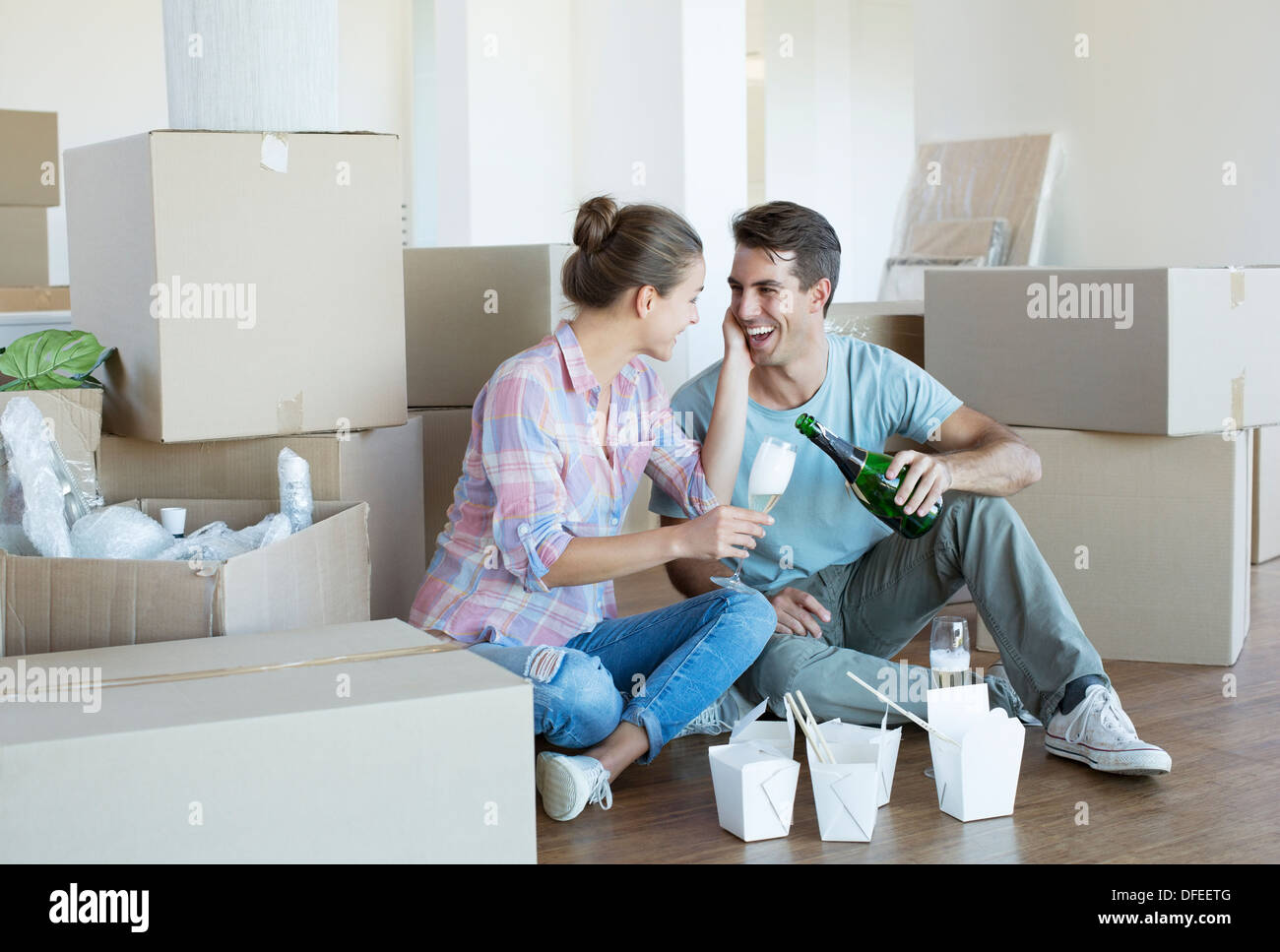 Couple drinking champagne and eating Chinese food on floor in new house Stock Photo