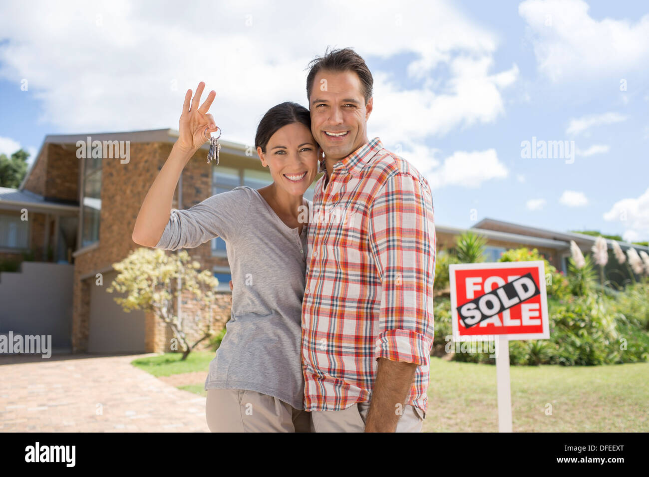 Portrait of smiling couple holding keys in front of new house Stock Photo