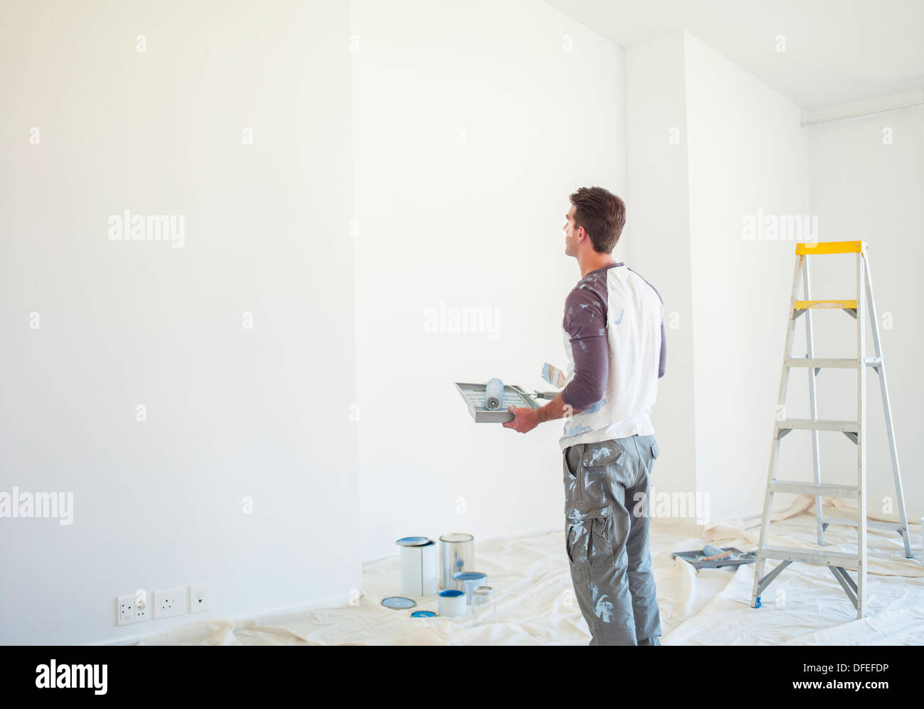 Man with paint tray looking up at white wall Stock Photo