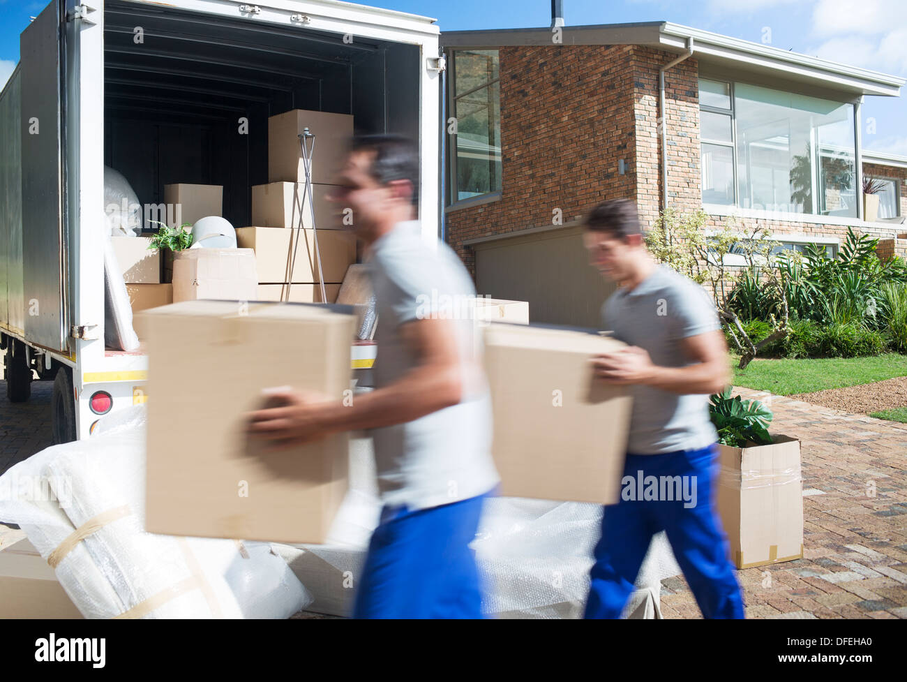 Movers carrying cardboard boxes in driveway past moving van Stock Photo
